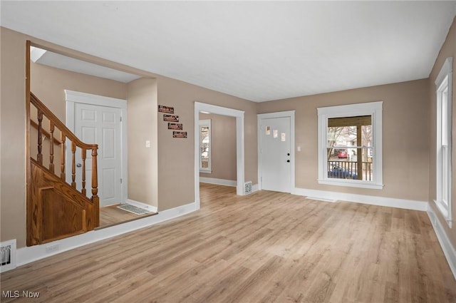 unfurnished living room with visible vents, baseboards, stairs, and light wood-style floors