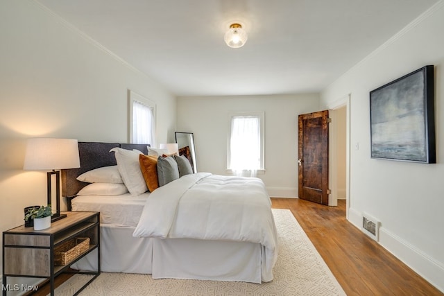 bedroom featuring baseboards, multiple windows, wood finished floors, and ornamental molding