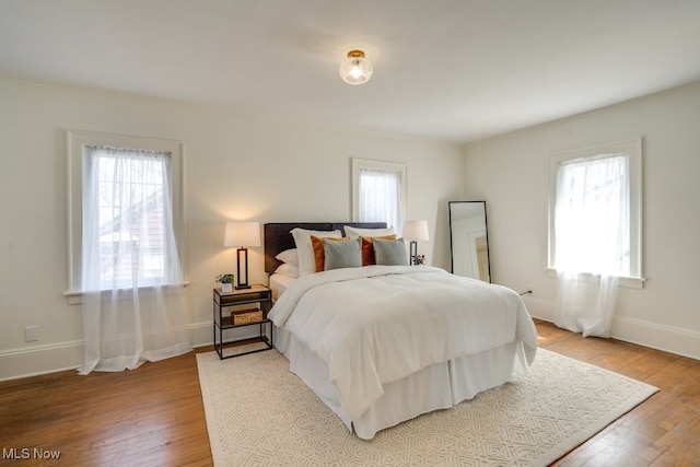 bedroom with baseboards, multiple windows, and light wood-style flooring