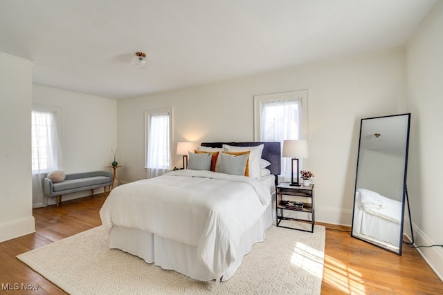 bedroom with baseboards, multiple windows, light wood-style floors, and ornamental molding