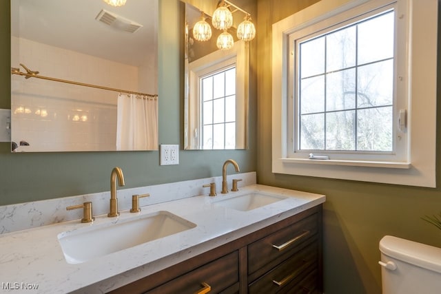 bathroom featuring a sink, visible vents, toilet, and double vanity