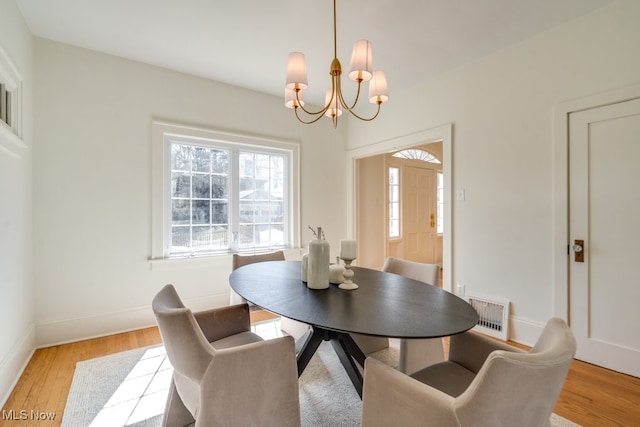 dining space with baseboards, light wood-type flooring, and a chandelier