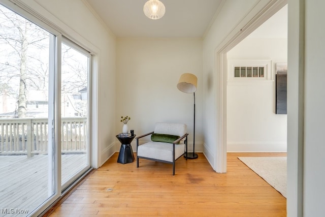 living area featuring baseboards, light wood-style flooring, and crown molding