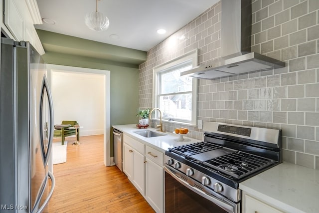 kitchen featuring tasteful backsplash, white cabinets, stainless steel appliances, wall chimney exhaust hood, and a sink