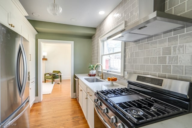 kitchen with wall chimney range hood, light countertops, appliances with stainless steel finishes, white cabinets, and a sink