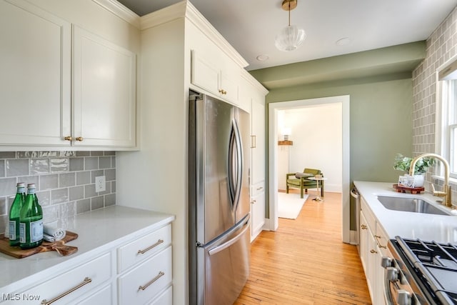 kitchen featuring light wood-style flooring, a sink, backsplash, appliances with stainless steel finishes, and light countertops