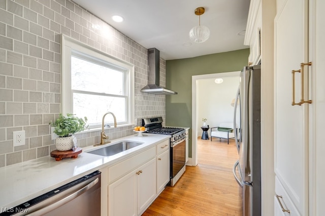 kitchen featuring light wood-style flooring, a sink, appliances with stainless steel finishes, wall chimney exhaust hood, and tasteful backsplash