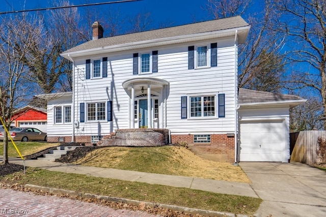 colonial home with driveway, a chimney, an attached garage, and a shingled roof