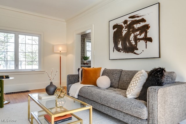 living area featuring baseboards, wood finished floors, visible vents, and ornamental molding