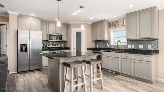 kitchen with gray cabinets, a sink, ornamental molding, stainless steel appliances, and a kitchen breakfast bar