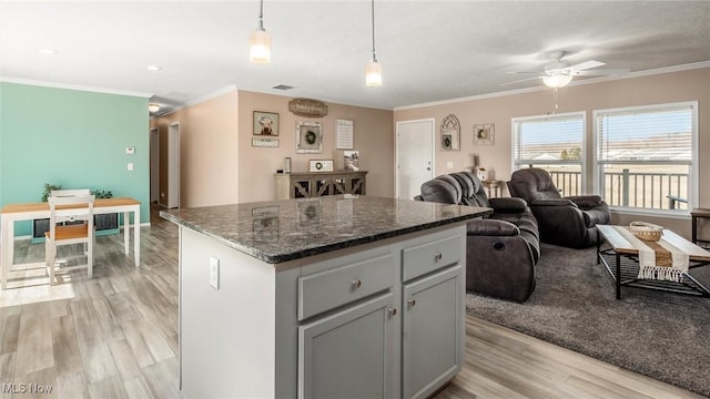 kitchen featuring light wood finished floors, a kitchen island, dark stone counters, ornamental molding, and ceiling fan