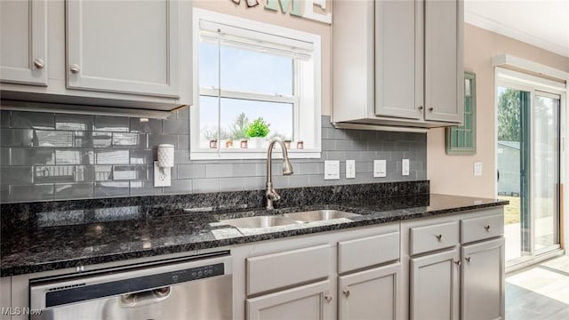 kitchen with dark stone counters, a sink, decorative backsplash, dishwasher, and crown molding