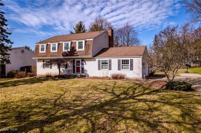 view of front facade with a shingled roof, a gambrel roof, a front yard, a chimney, and driveway