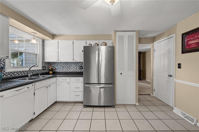 kitchen with visible vents, white dishwasher, freestanding refrigerator, a sink, and dark countertops