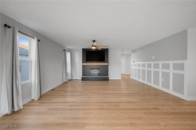 unfurnished living room with light wood-style flooring, a brick fireplace, baseboards, and ceiling fan