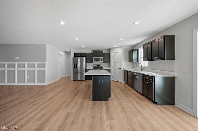 kitchen with a sink, a kitchen island, light wood-style floors, appliances with stainless steel finishes, and light countertops