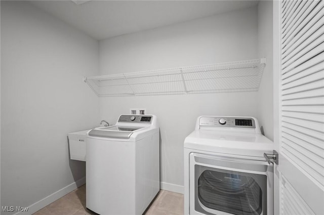 clothes washing area featuring light tile patterned floors, baseboards, laundry area, a sink, and washer and clothes dryer