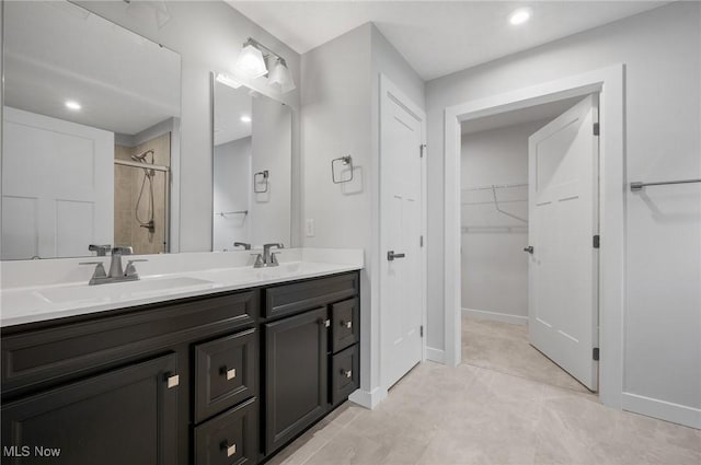 full bath with double vanity, a shower stall, a walk in closet, and a sink