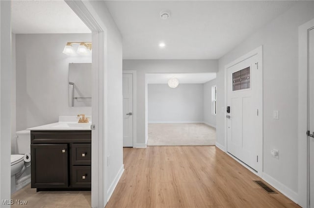 hall with light wood-type flooring, visible vents, baseboards, and a sink