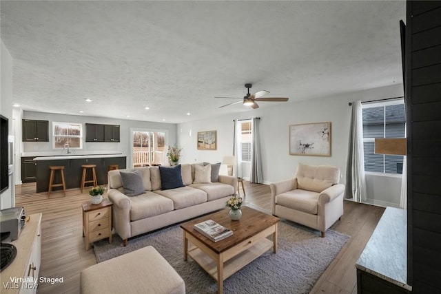 living area with recessed lighting, light wood-style floors, a ceiling fan, and a textured ceiling