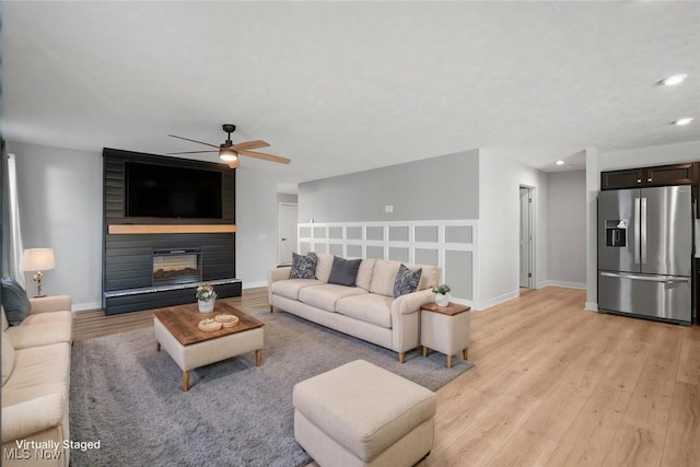 living room with baseboards, ceiling fan, recessed lighting, a fireplace, and light wood-style floors