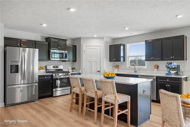 kitchen featuring a breakfast bar area, a sink, light countertops, light wood-style floors, and appliances with stainless steel finishes