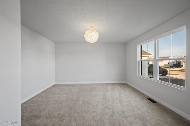 carpeted spare room with visible vents, an inviting chandelier, a textured ceiling, and baseboards