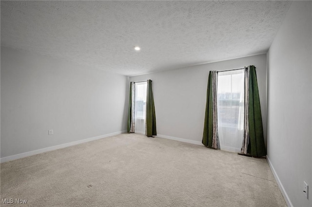 empty room featuring baseboards, light carpet, and a textured ceiling