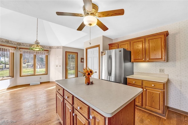 kitchen featuring a center island, wallpapered walls, light wood-type flooring, freestanding refrigerator, and brown cabinetry