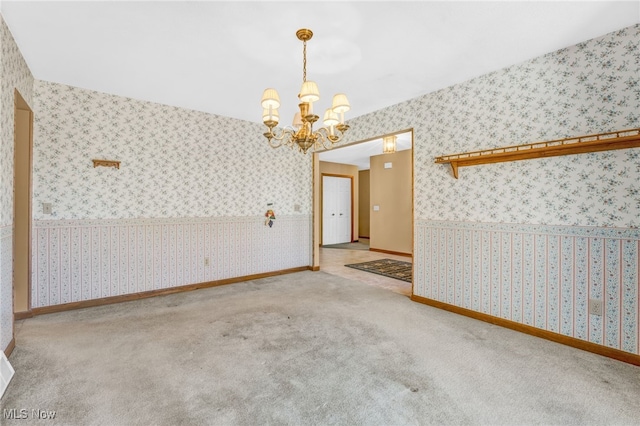 carpeted empty room featuring baseboards, an inviting chandelier, and wallpapered walls