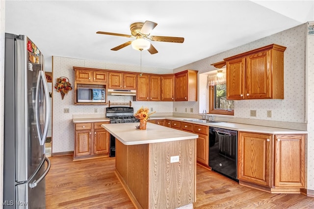 kitchen featuring wallpapered walls, under cabinet range hood, appliances with stainless steel finishes, light wood-style floors, and a sink