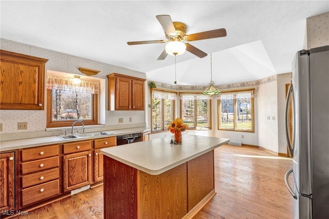 kitchen featuring brown cabinets, wallpapered walls, freestanding refrigerator, and a sink