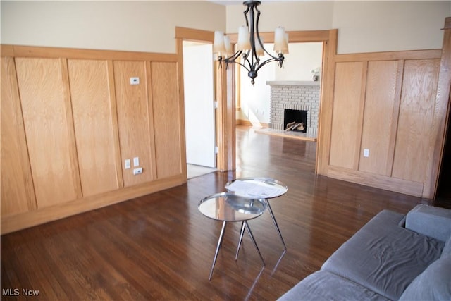 living area with a notable chandelier, a brick fireplace, and dark wood finished floors