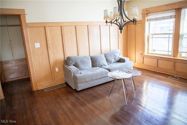 living area with dark wood finished floors, an inviting chandelier, visible vents, and wainscoting