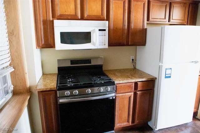 kitchen featuring light stone counters, white appliances, and brown cabinetry