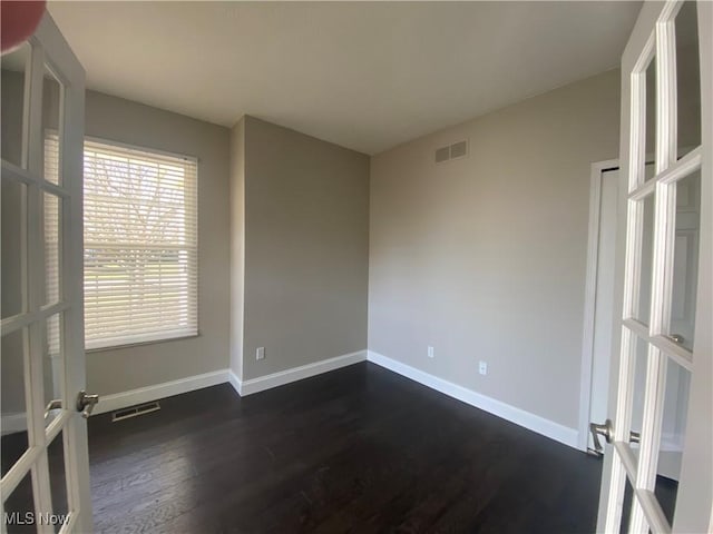 empty room featuring visible vents, dark wood-type flooring, and baseboards