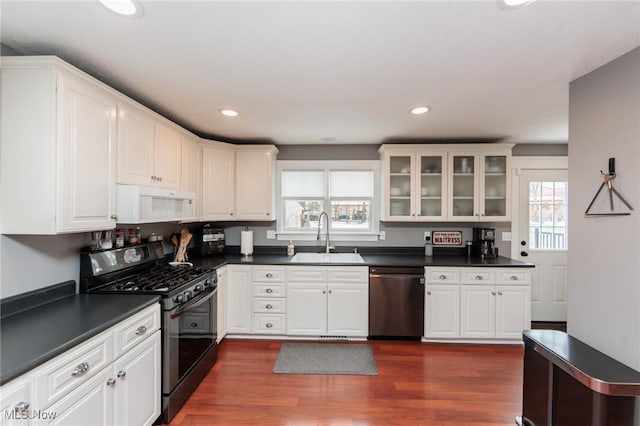 kitchen with a sink, stainless steel dishwasher, dark countertops, gas stove, and white microwave