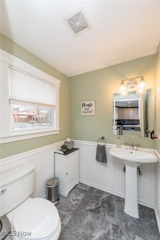 bathroom with a sink, toilet, visible vents, and wainscoting