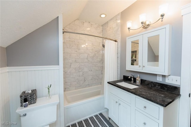 full bath featuring vanity, a wainscoted wall, vaulted ceiling, shower / tub combo, and toilet