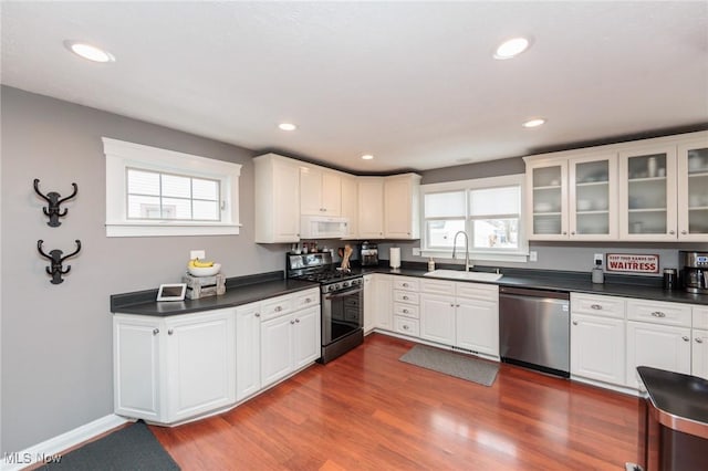 kitchen with dark wood finished floors, a sink, stainless steel appliances, white cabinets, and dark countertops