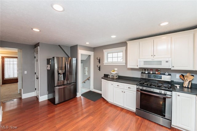 kitchen with dark wood-type flooring, dark countertops, appliances with stainless steel finishes, and white cabinetry