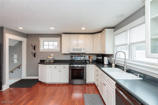 kitchen featuring dark countertops, stainless steel appliances, dark wood-style floors, white cabinetry, and a sink