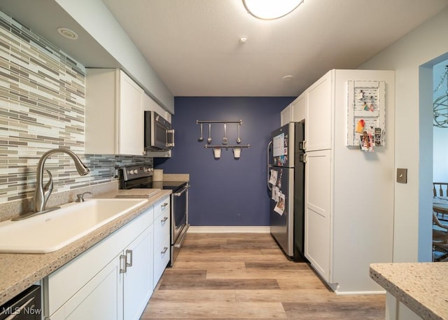 kitchen featuring light wood-type flooring, a sink, stainless steel appliances, white cabinetry, and tasteful backsplash