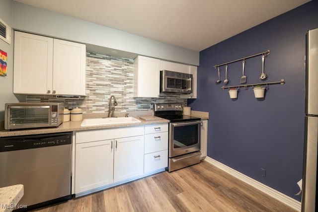 kitchen featuring tasteful backsplash, light countertops, appliances with stainless steel finishes, white cabinets, and a sink