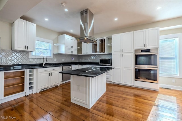 kitchen with open shelves, light wood-style floors, island range hood, stainless steel appliances, and a sink