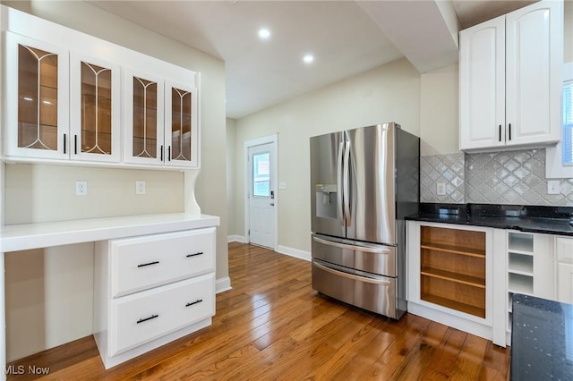 kitchen with stainless steel refrigerator with ice dispenser, hardwood / wood-style flooring, tasteful backsplash, white cabinets, and glass insert cabinets