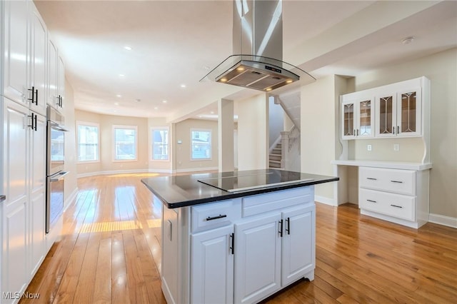 kitchen with black electric stovetop, island exhaust hood, light wood-style floors, and a kitchen island