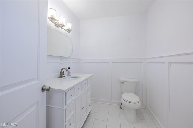 bathroom with wainscoting, a decorative wall, toilet, and vanity