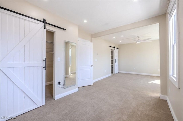 unfurnished bedroom with recessed lighting, a barn door, carpet flooring, baseboards, and a spacious closet