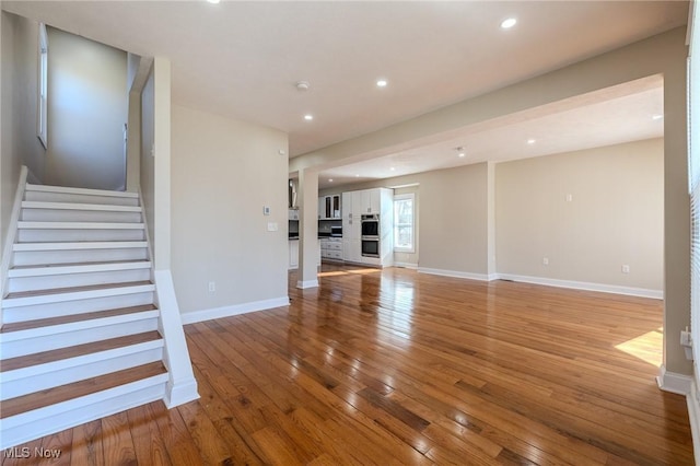 unfurnished living room featuring recessed lighting, baseboards, wood-type flooring, and stairway